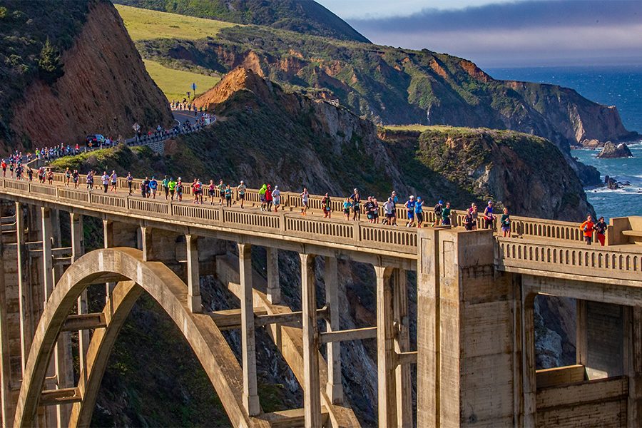 A wide shot runners running on a long road on the Big Sur International Marathon trail in California